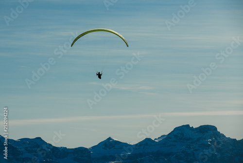 Paraglider in silhouette flies paraglide above beautiful snow capped mountains. Alta Badia, South Tyrol, Dolomites, Italy