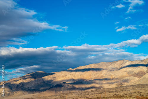 blue sky white clouds cast shadows over light tone desert hills in Eastern Sierra Nevada  California  USA
