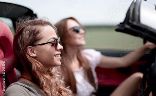 two fashionable girls travel in a convertible car.