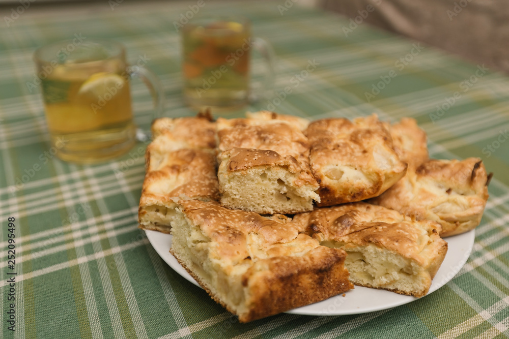 Slices of apple cake Charlotte on a plate with two glasses of tea. Table covered with green tablecloth
