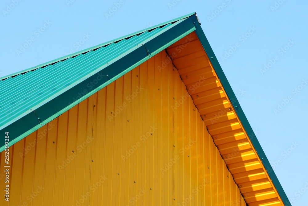 attic of yellow plastic wall and green roof against the sky attic of yellow plastic wall and green roof against the sky