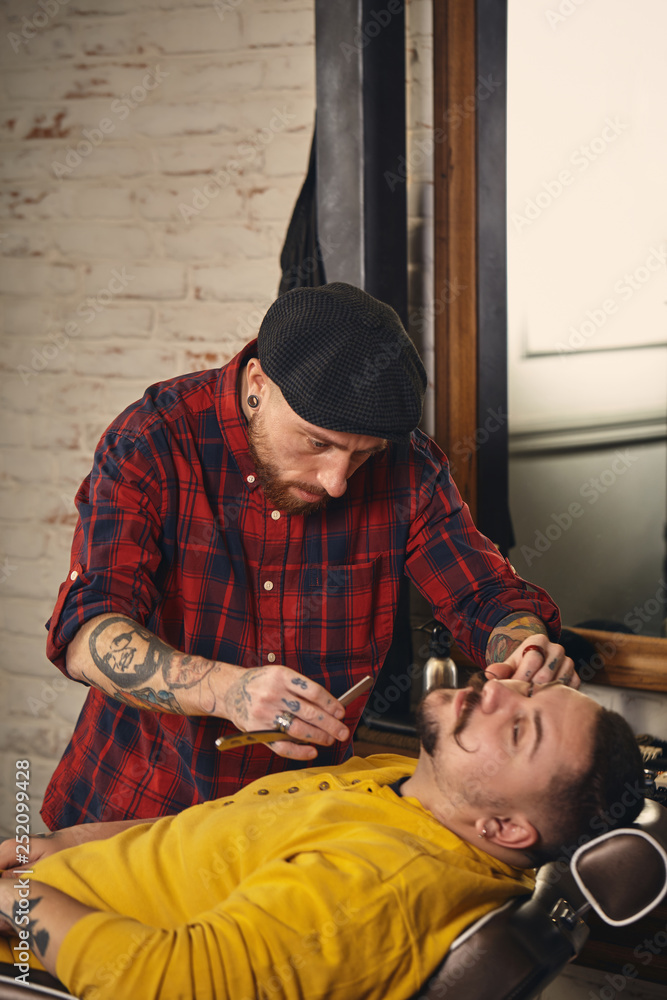 Fototapeta premium Client during beard shaving in barber shop