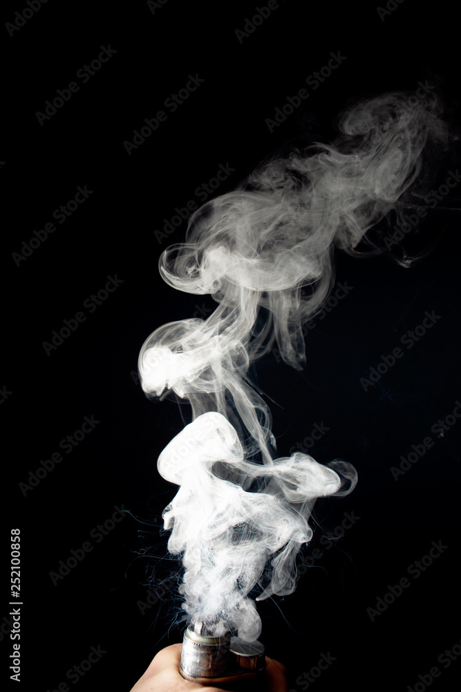 Male hand holds vape without atomiser. Column of vape clouds splash from coil on black background. Fog is white. Stock isolated white smoke with spray boiling glycerine. Male hand holds vape without atomiser. Column of vape clouds splash from coil on black background. Fog is white. Stock isolated white smoke with spray boiling glycerine.