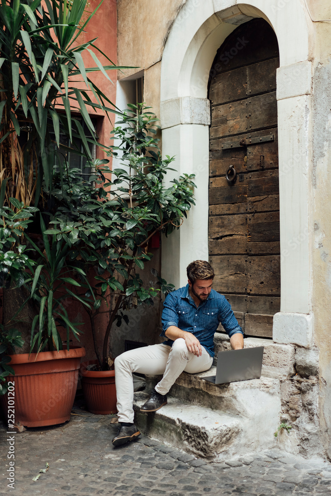 Businessman sitting on steps in a courtyard using laptop Businessman sitting on steps in a courtyard using laptop