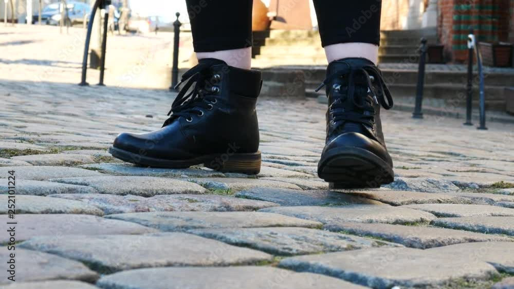 Close up women's feet in black boots on cobblestone pavement Close up women's feet in black boots on cobblestone pavement