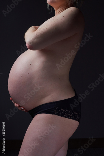 A beautiful pregnant woman body  with the woman gently holding and supporting the pregnant stomach. Gentle feminine motherhood. Photographed on a black studio background.