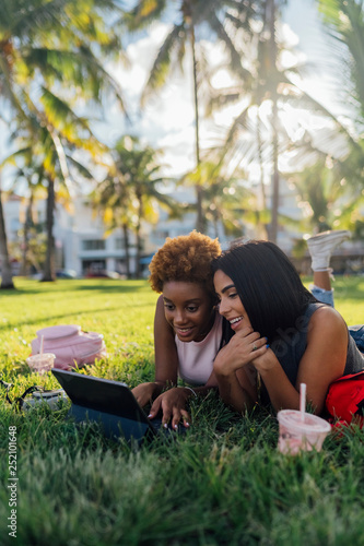 Two happy female friends relaxing in a park using a tablet