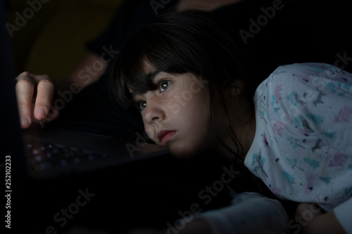 Portrait of daughter watching father using laptop on couch at night