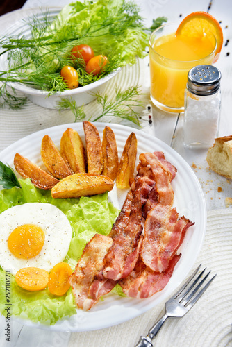 Food on the table. Breakfast with bacon. Fried bacon with. French fries and tender egg, and a glass of fresh juice.