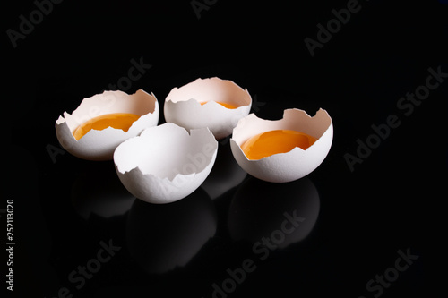 Raw white broken eggs in eggshell halves on black background
