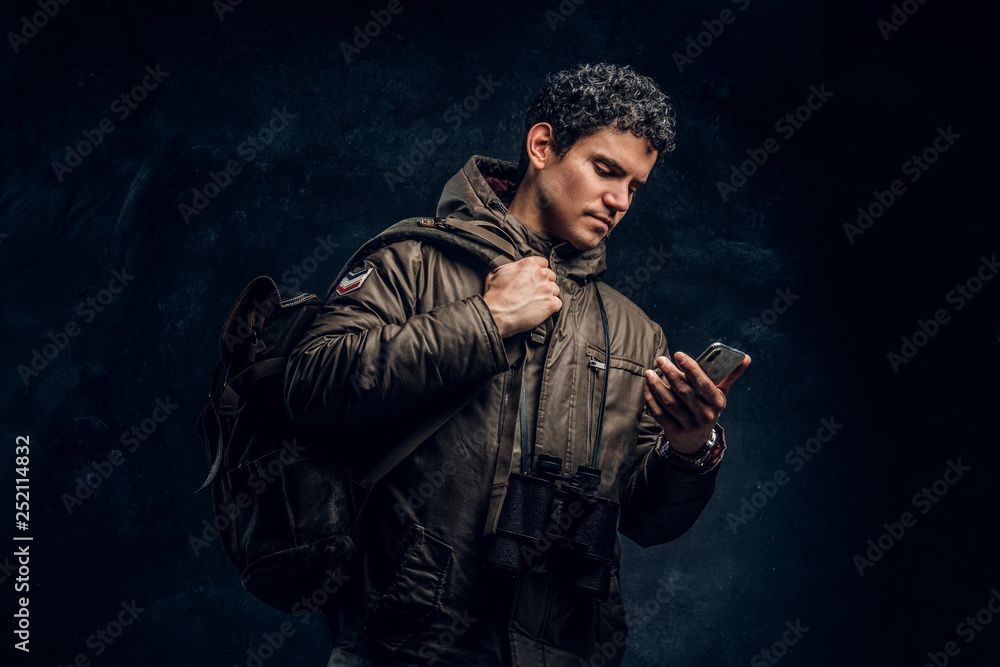 Serious traveler with binoculars looking into the phone pictured sideways on a black background