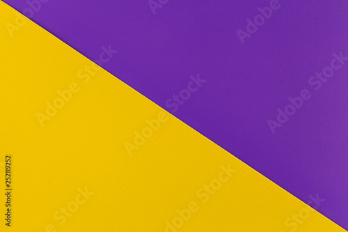 Vibrant yellow and purple colored plastic surfaces jointed diagonally, background.