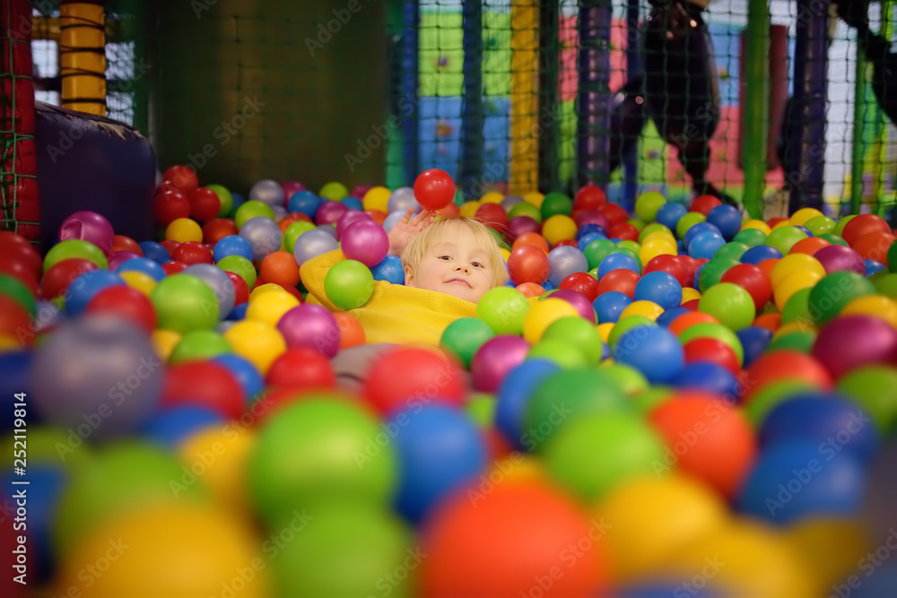 Happy little boy having fun in ball pit with colorful balls. Child playing on indoor playground.