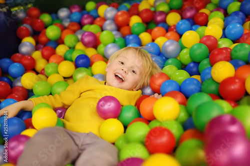 Happy little boy having fun in ball pit with colorful balls. Child playing on indoor playground.
