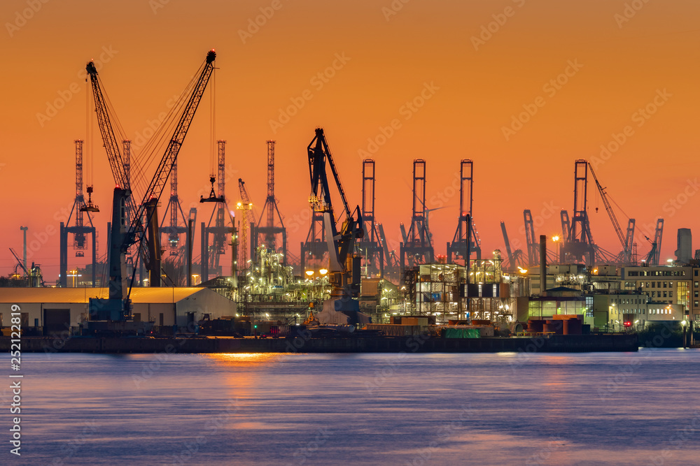 Obraz premium Cranes silhouetted against the evening sky in Hamburg Harbor, Germany, at dusk. The Port of Hamburg (Hamburger Hafen) is a sea port on the river Elbe. It is Germany's largest harbor.