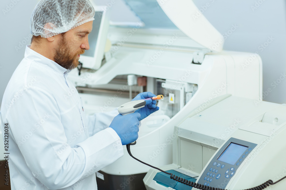Male medical worker with bread working with new equipment. Handsome laboratory assistant in lab coat checking results of experiment. Doctor holding test tubes and seriously typing on touch screen. Male medical worker with bread working with new equipment. Handsome laboratory assistant in lab coat checking results of experiment. Doctor holding test tubes and seriously typing on touch screen.