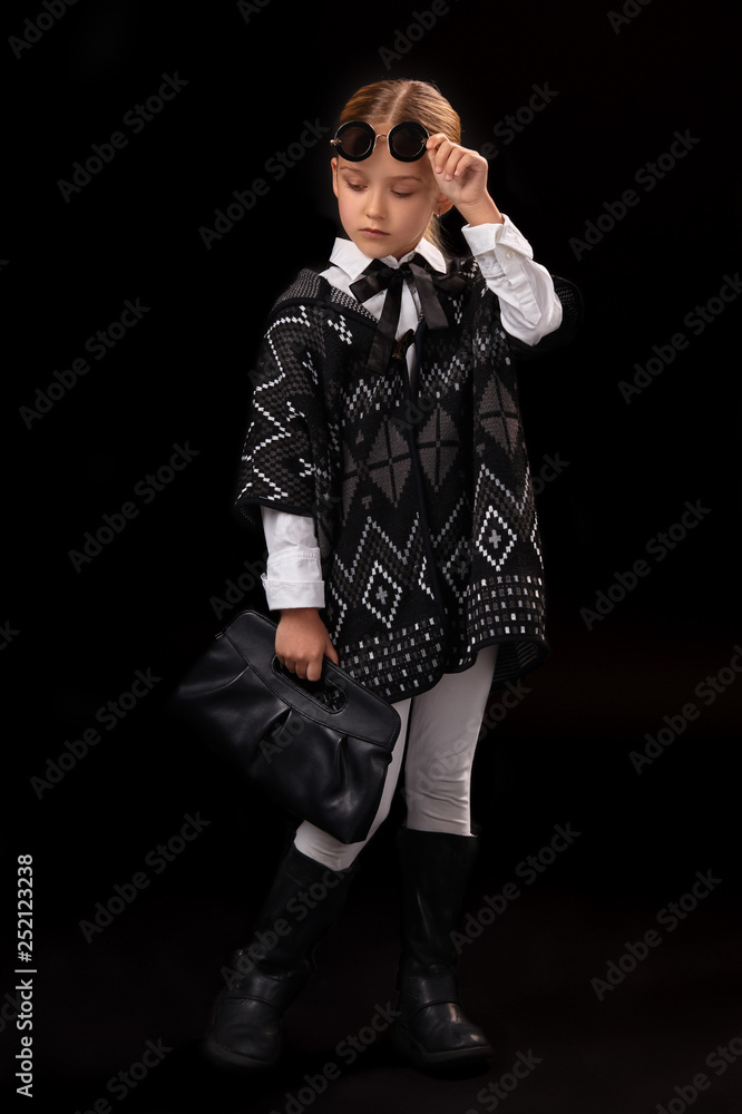 Plakat Mała dziewczynka w czarnych okularach, ciemnym poncho, czarnych butach i sprzęgle w dłoni