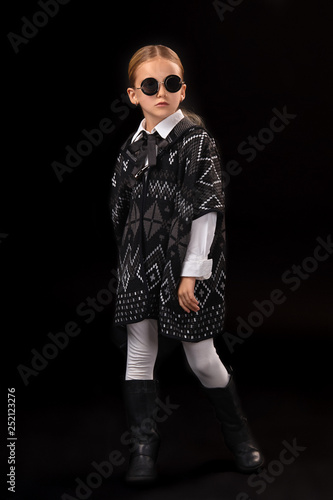 Little girl in a black glasses, dark poncho, black boots and a clutch in her hand © nazarovsergey