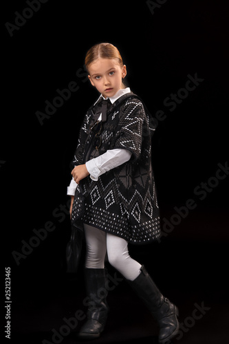 Little girl in a dark poncho, black boots and a clutch in her hand photo