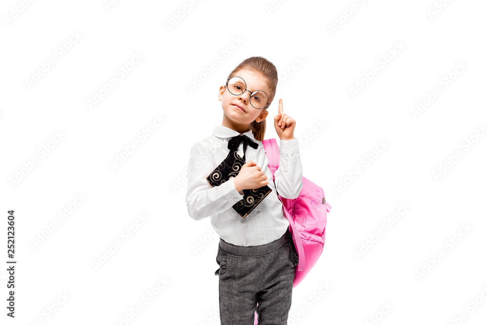 Back to school. Beautiful little girl dressed like a School girl - in white shirt and gray pants, rounded glasses, hold a book, school bag and posing like model points finger up. Isolated on white. Back to school. Beautiful little girl dressed like a School girl - in white shirt and gray pants, rounded glasses, hold a book, school bag and posing like model points finger up. Isolated on white.