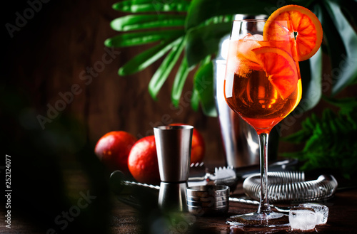 Aperol spritz cocktail in big wine glass with bloody oranges  summer Italian fresh alcohol cold drink. Wooden bar counter background with tools  summer mood concept with palm trees  selective focus