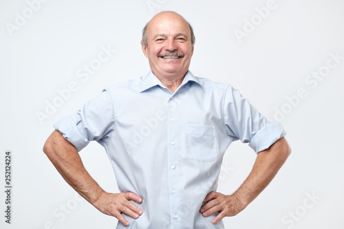 senior man with a proud, satisfied and happy look, with both hands on hips