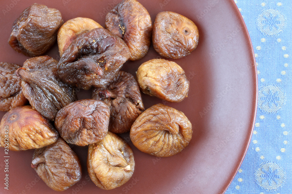 Dried figs on a brown ceramic plate on blue tablecloth