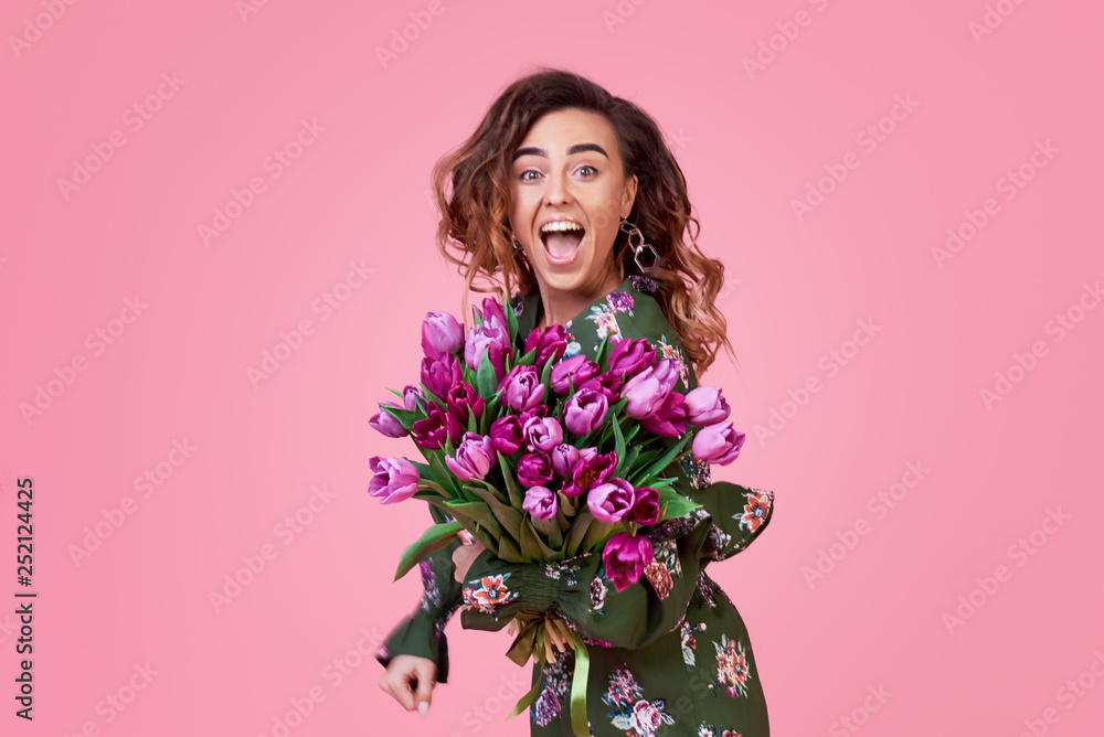 Cheerful and joyful young redhead woman in fashionable green dress being excited to get bouquet of spring yellow flowers tulips on women's day isolated over pink background. Gift Surprise Effect Cheerful and joyful young redhead woman in fashionable green dress being excited to get bouquet of spring yellow flowers tulips on women's day isolated over pink background. Gift Surprise Effect