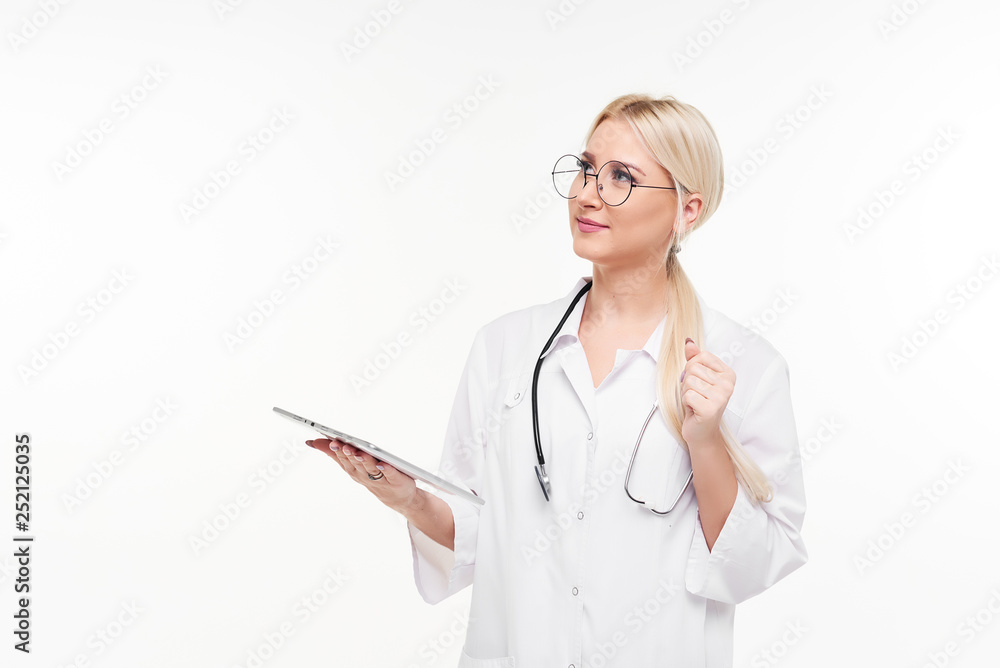 Portrait of young female blond doctor in white working uniform looking at camera isolated on white. A stethoscope is hanging on the neck. Looks left, space for text. Portrait of young female blond doctor in white working uniform looking at camera isolated on white. A stethoscope is hanging on the neck. Looks left, space for text.