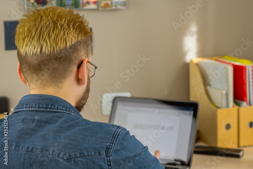 Back view of unrecognizable male freelancer using laptop to work remotely from home