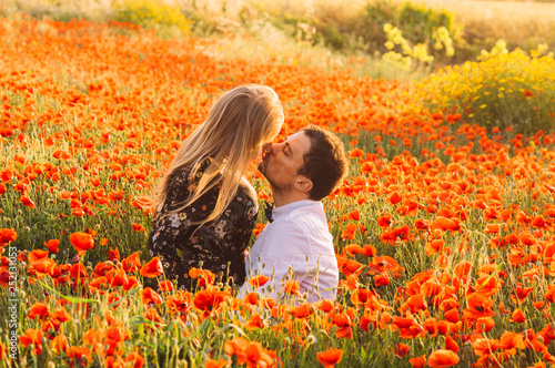 Man and woman embracing and kissing in poppy field on the dusk