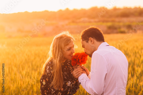 Man and woman smells bouquet of poppies in wheat field on the dusk