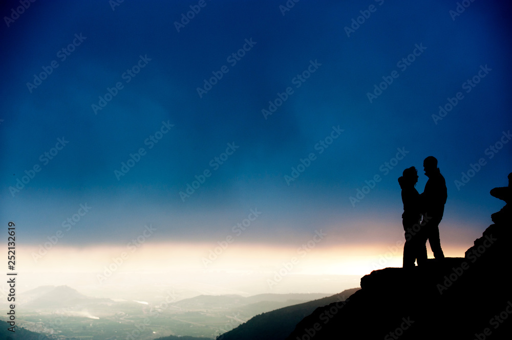 Silueta de pareja besándose en roca junto paisaje al atardecer