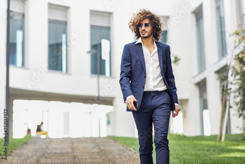 Portrait of young fashionable businessman with curly hair wearing blue suit and sunglasses photo