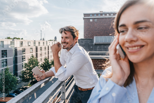 Business people standing on balcony, using smartphone