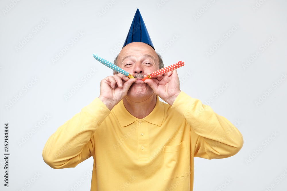 Senior man blowing party horn and staring at camera having excited look  while celebrating birthday foto de Stock | Adobe Stock