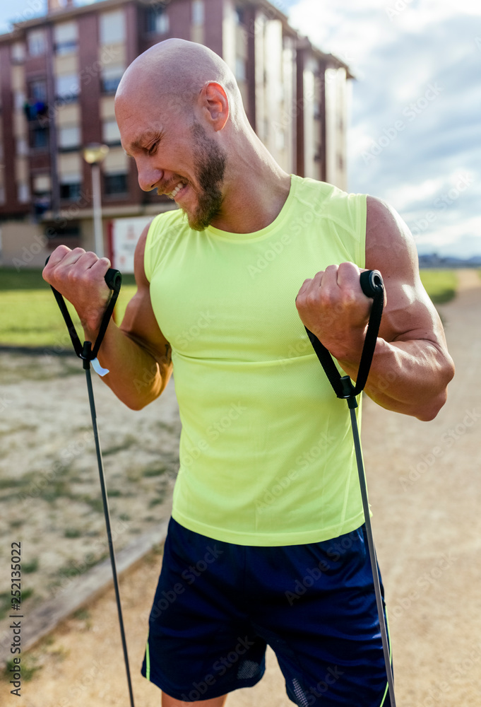 Muscular man exercising with expander outdoors Muscular man exercising with expander outdoors
