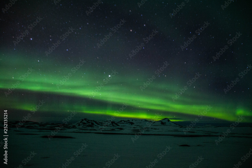 Winter scenic landscape night view of  Aurora Borealis/Northern lights dancing on the clear sky full of stars above snow covered mountains. Mývatn, North Iceland. Beautiful winter background scene. 