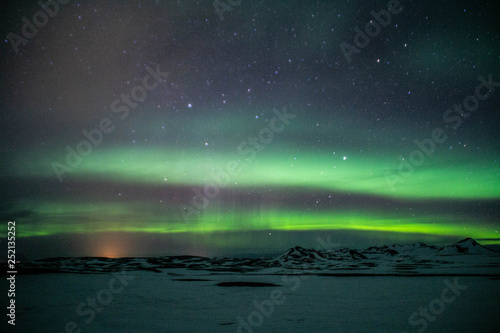 Winter scenic landscape night view of Aurora Borealis/Northern lights dancing on the clear sky full of stars above snow covered mountains. Mývatn, North Iceland. Beautiful winter background scene. 