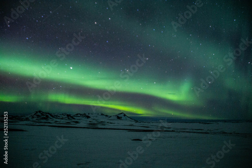 Winter scenic landscape night view of Aurora Borealis/Northern lights dancing on the clear sky full of stars above snow covered mountains. Mývatn, North Iceland. Beautiful winter background scene. 