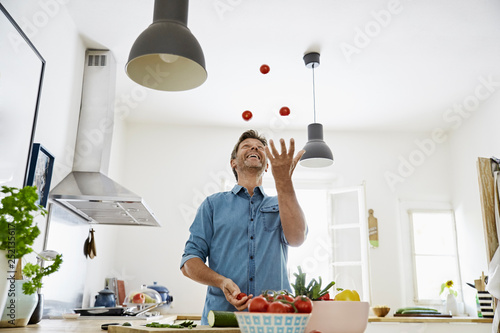 Mature man standing in kitchen, juggling with tomatoes photo