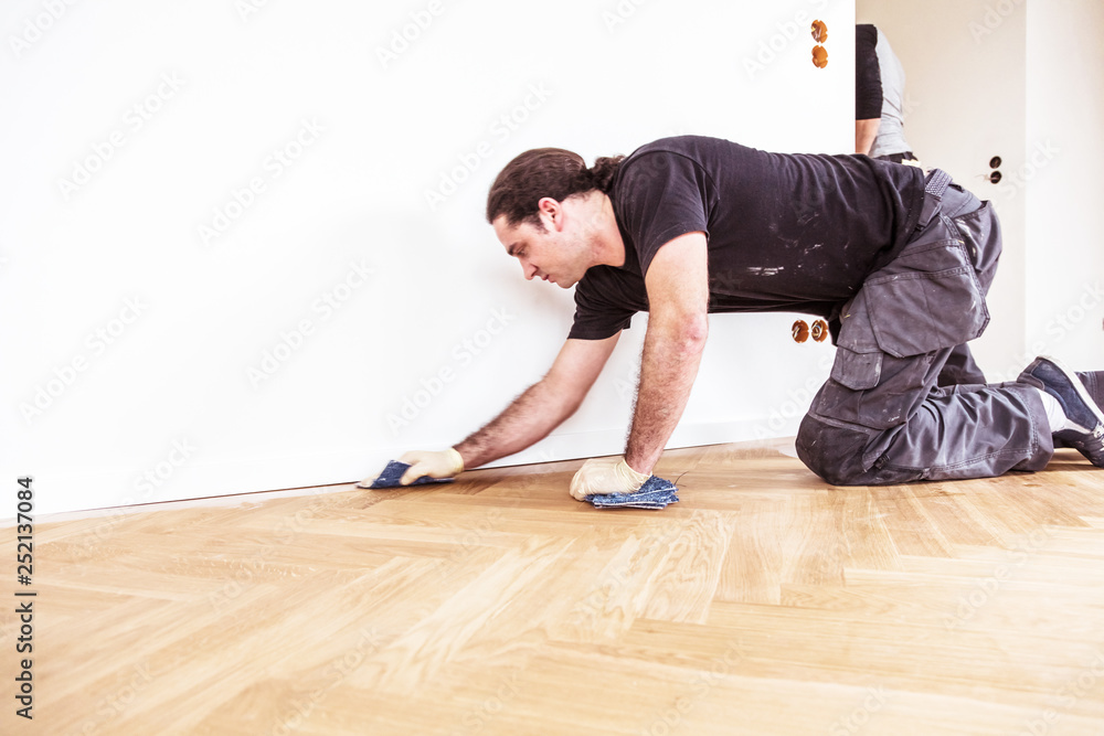 Male hand cleaning and rubbing an hardwood floor with a microfiber cloth - obrazy, fototapety, plakaty 