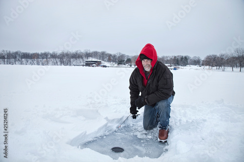 A smiling middle aged man ice fishing on a lake in Minnesota during winter