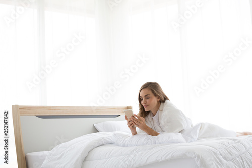 Relaxed caucasian woman using a smartphone in the morning on the bed in the bedroom at home