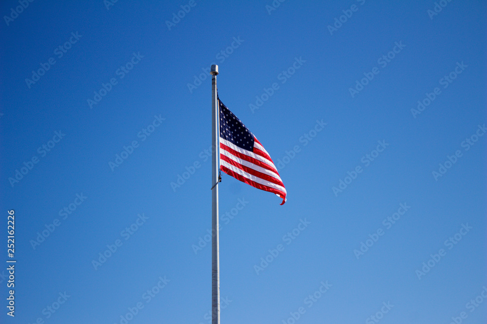 American flag in a light breeze with solid blue sky background