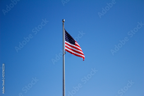 American flag in a light breeze with solid blue sky background