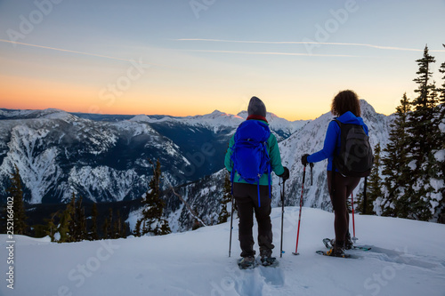 Couple friends are snowshoeing on top of a mountain during a vibrant winter sunset. Taken on top of Zoa Peak near Hope, British Columbia, Canada.