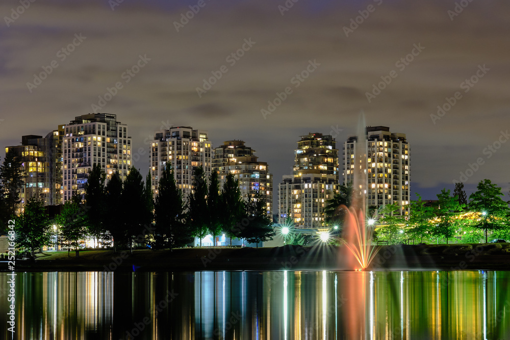 custom made wallpaper toronto digitalNight scape city view, Coquitlam, Greater Vancouver area, Canada. Fountain in lake and water reflections of modern buildings windows lights