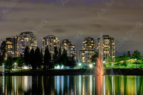 Night scape city view  Coquitlam  Greater Vancouver area  Canada. Fountain in lake and water reflections of modern buildings windows lights