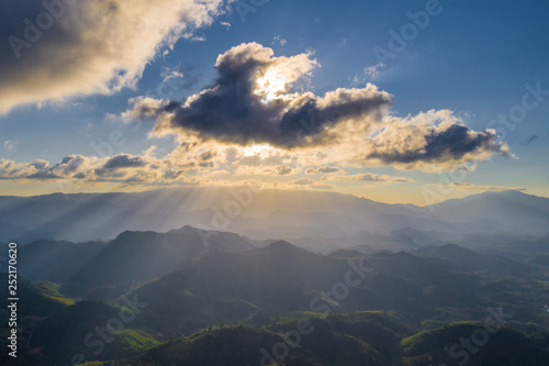Sunset sun hidden by the clouds shinning on the distant mountain range silhouettes drone top view